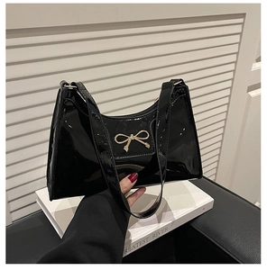 Detail of a black patent leather crescent bag featuring a golden bow and sleek zipper