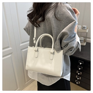 Detail of square white handbag showing vertical texture, handles and crossbody strap