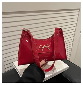 Detail of red patent leather crescent bag with gold metal bow and smooth zipper closure
