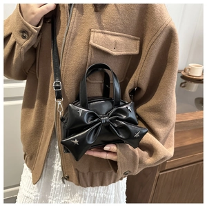 Détail d'un sac à main noir avec un grand nœud papillon et des rivets en forme d'étoile