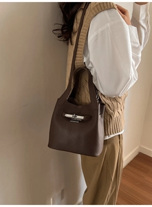 Détail du sac seau en cuir marron foncé avec fermoir rotatif argenté porté par un mannequin