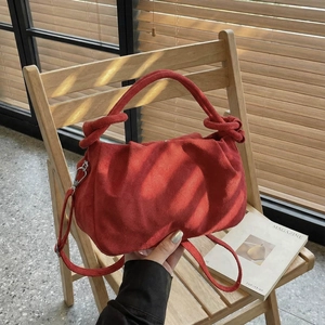 Elegant red pleated suede handbag for women, shown on a wooden chair with natural light