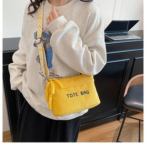 Detail of yellow corduroy tote bag with black embroidery and striped shoulder strap
