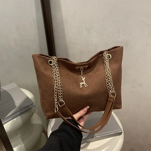 Deep brown textured tote bag with golden chain strap and deer charm in a studio setting