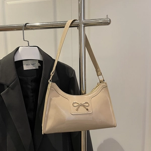 Chic beige patent leather crescent shoulder bag with metallic bow detail and top zipper