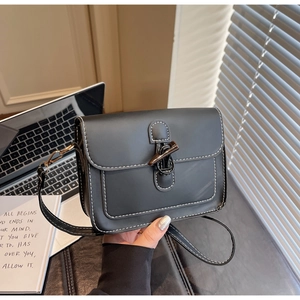 Detail of black crossbody bag featuring white contrast stitching and a horn button closure