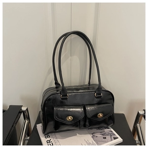Close-up of black glossy handbag with golden twist-lock front pockets and twin handles