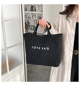 Detail of a black tote bag with white text print held by a model in a bright room