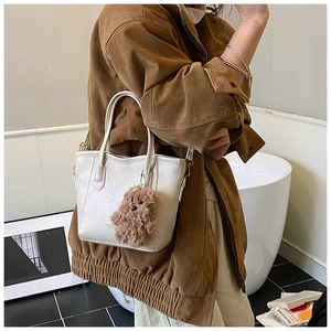 Detail of cream white bucket bag featuring a cute brown plush bear charm and dual handles