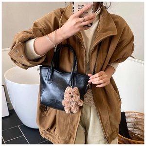 Detail of black textured tote bag with brand lettering and brown plush dog pendant charm