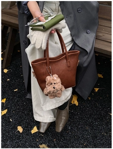 Brown leather tote bag with plush dog charm held by model in autumn outdoor setting