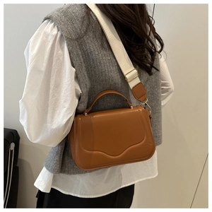 Brown leather crossbody bag with wave edge flap and wide cream textile strap on model
