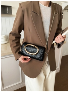 Detail of black crocodile embossed leather bag featuring a large gold ring buckle and chain