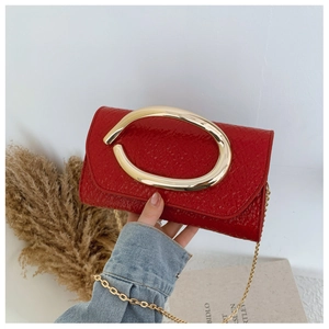 Detail of red embossed leather handbag with gold ring handle and metal chain strap