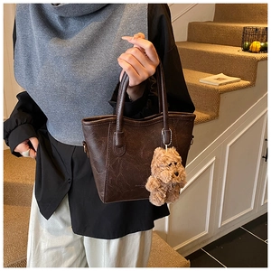 Deep brown tote bag with vintage cracked leather texture and a plush bear pendant charm