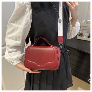 Close-up of red leather square handbag with contrast wide strap and metallic closure