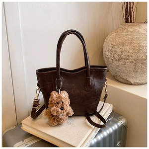 Close-up of a dark brown retro tote bag with a plush puppy charm on a silver suitcase