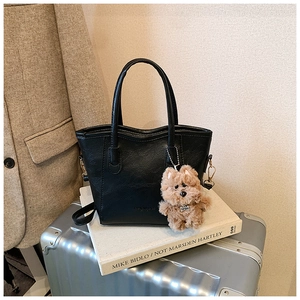 Close-up of black textured tote bag with brown plush puppy charm on art books
