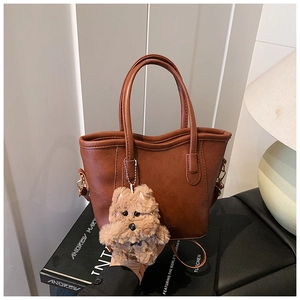 Detail of a brown leather tote bag featuring a cute plush dog pendant and shoulder strap