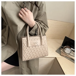Detail of apricot quilted handbag with metal bow on khaki trench coat background