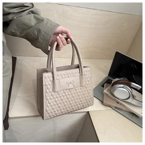 Close-up of beige quilted tote bag with bow detail in a minimalist office setting