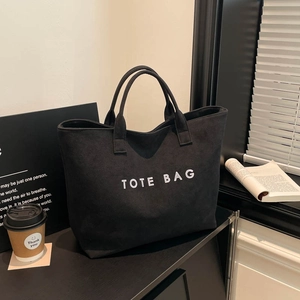 Minimalist black canvas tote bag with bold TOTE BAG text print in modern office setting