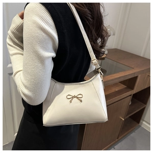 Detail of a creamy white shoulder bag with a polished golden bow hardware and leather texture