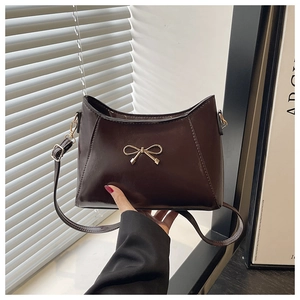 Detail of dark brown glossy leather shoulder bag with golden bow hardware and strap