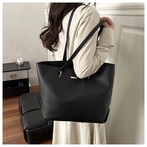 Model wearing a black oversized matte leather tote bag with gold logo in a French room