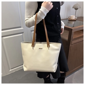 Détail du sac fourre-tout blanc cassé avec anses marron et logo doré dans un intérieur chic