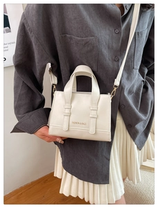 Detail showing the white leather square bag with golden lettering and metal strap clasp
