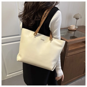 Detail of silver metal logo on off-white faux leather tote bag with brown straps
