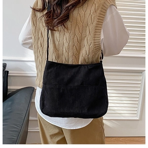 Detail view of black corduroy crossbody bag with front pocket on a casual outfit