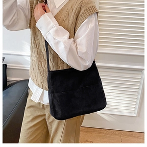 Close-up of black corduroy shoulder bag showing vertical rib texture and front pocket detail