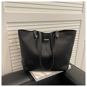 Détail du sac cabas en cuir noir minimaliste avec plaque logo dorée sur un décor moderne