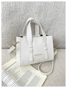 Close-up of a white PU leather tote bag on textured fabric with vintage paper accents