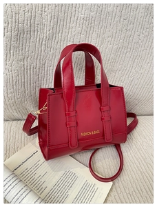 Close-up of bright red PU leather handbag with golden hardware on a soft textured sofa