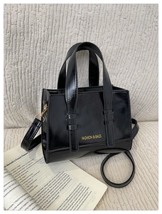 Detail of a black PU leather handbag with gold lettering on a beige textured sofa