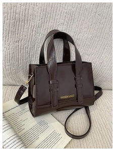 Detail of a dark brown glossy PU leather handbag with gold hardware and shoulder strap