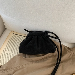 Detailed view of black pleated suede cloud bag on an open book with soft textures