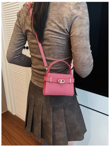 Close-up of fuchsia lychee leather handbag with golden turn-lock and detachable strap