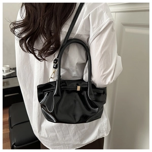 Modella indossa una borsa a secchiello plissettata nera lucida con dettagli dorati e fibbie