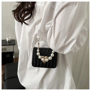 Close-up of black crossbody bag featuring pearl-studded heart buckle and gold chain strap