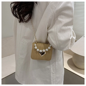 On-body view of a khaki woven crossbody bag featuring pearl handle and heart-shaped clasp