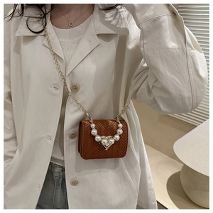 Detail of brown woven crossbody bag featuring pearl handle and gold heart clasp on model