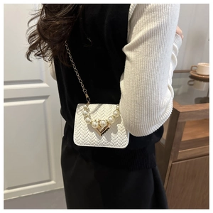 Detail of woven texture, pearl handle, and gold chain strap on white crossbody bag