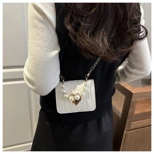 Close-up of woven white crossbody bag featuring pearl handle and gold heart lock