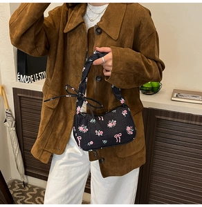 Close-up of a black embossed handbag with pink floral and bow patterns held by a model