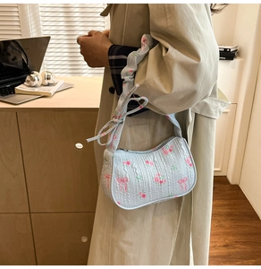 Close-up of light blue drawstring bag with floral patterns and bow details on a model