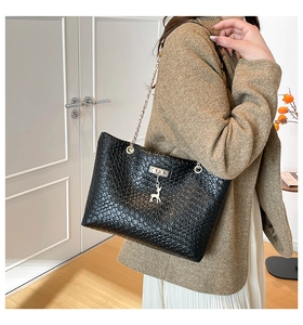 Detail of woven texture black tote bag with gold deer pendant and metal chain strap